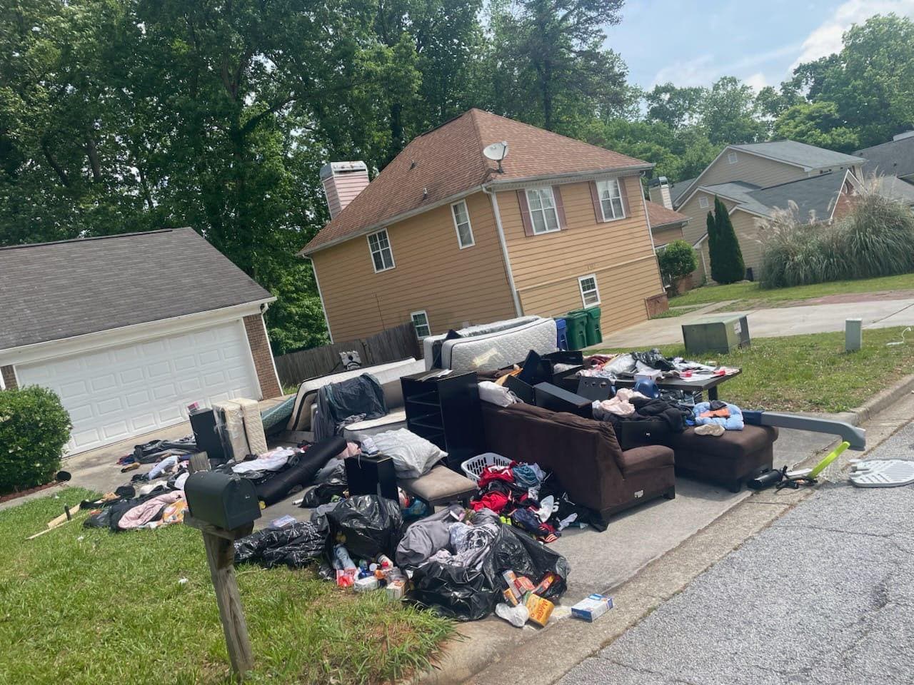 Large curbside pile before removal with furniture, mattresses, clothing, and bagged trash staged for a whole-house cleanout.