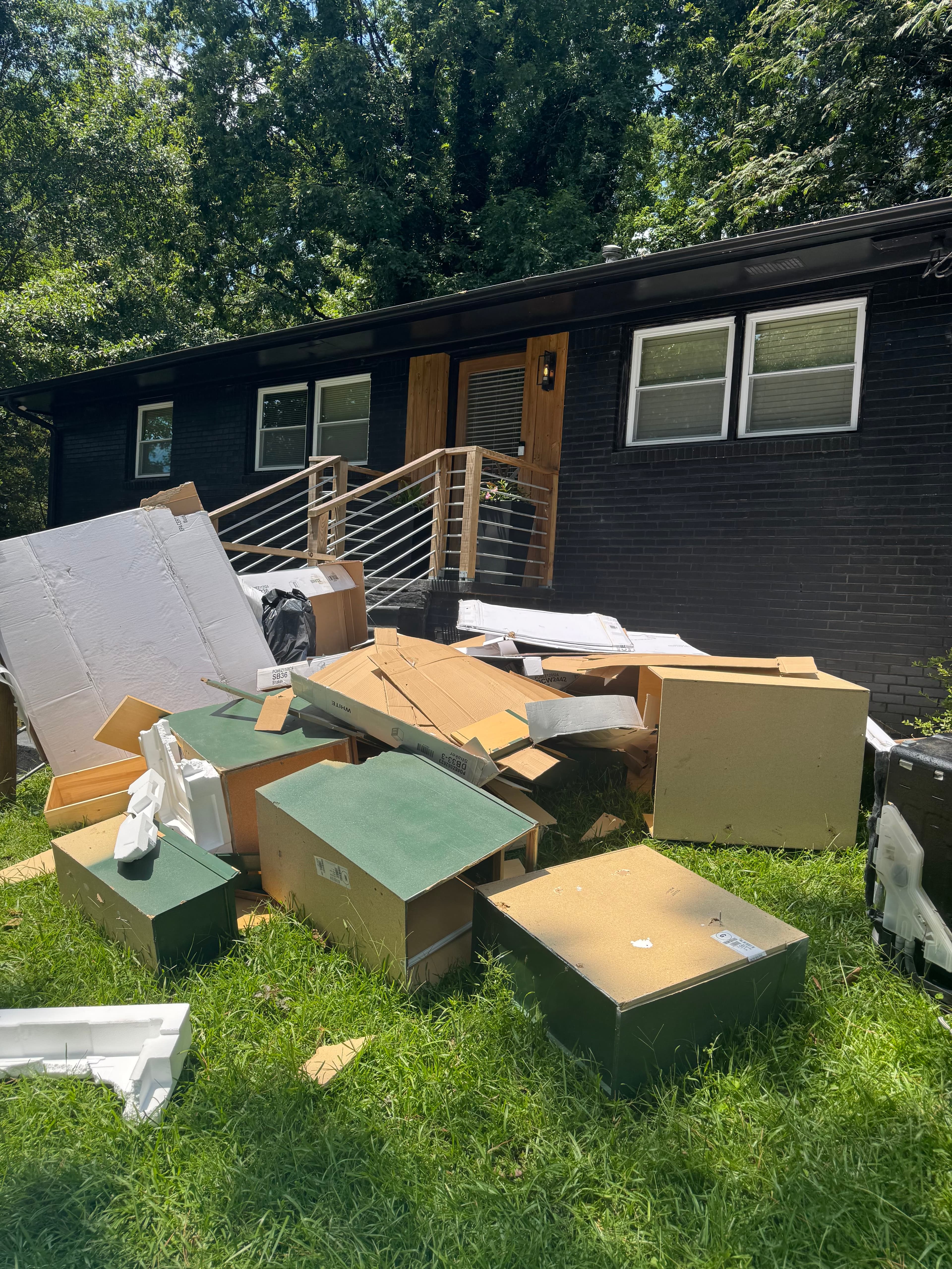 Exterior before photo showing cardboard, broken cabinets, and mixed debris piled in front of a home.
